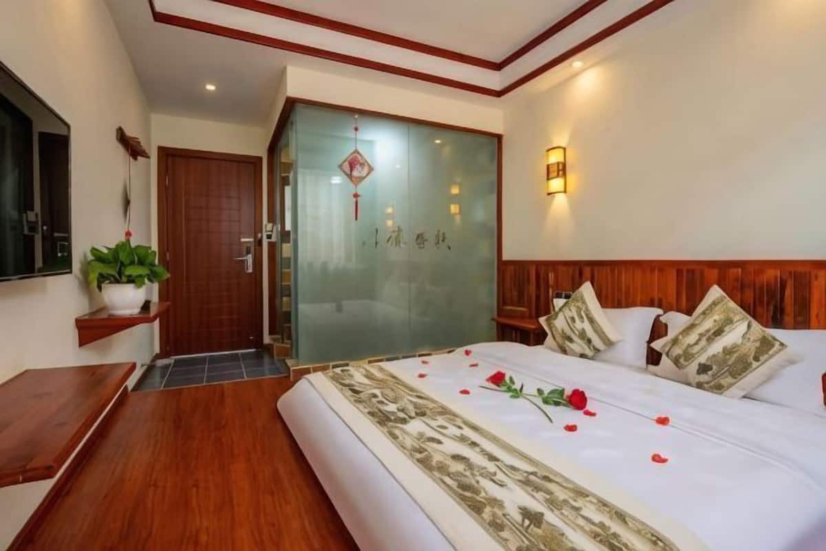 A hotel room with a bed, wooden headboard, bedside tables, a potted plant, and a sliding door with a decorative emblem.