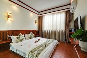 A hotel room with a bed, bedside tables, a TV, a plant, and a window with curtains. - Pu'er Shihoude Inn (Pu'er)