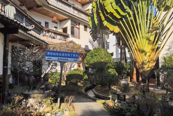 A pathway leading to a building with a traditional architectural style, surrounded by various plants and a large palm tree.