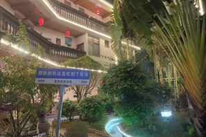 A building with a sign in Chinese, surrounded by greenery and illuminated by string lights. - Pu'er Shihoude Inn (Pu'er)