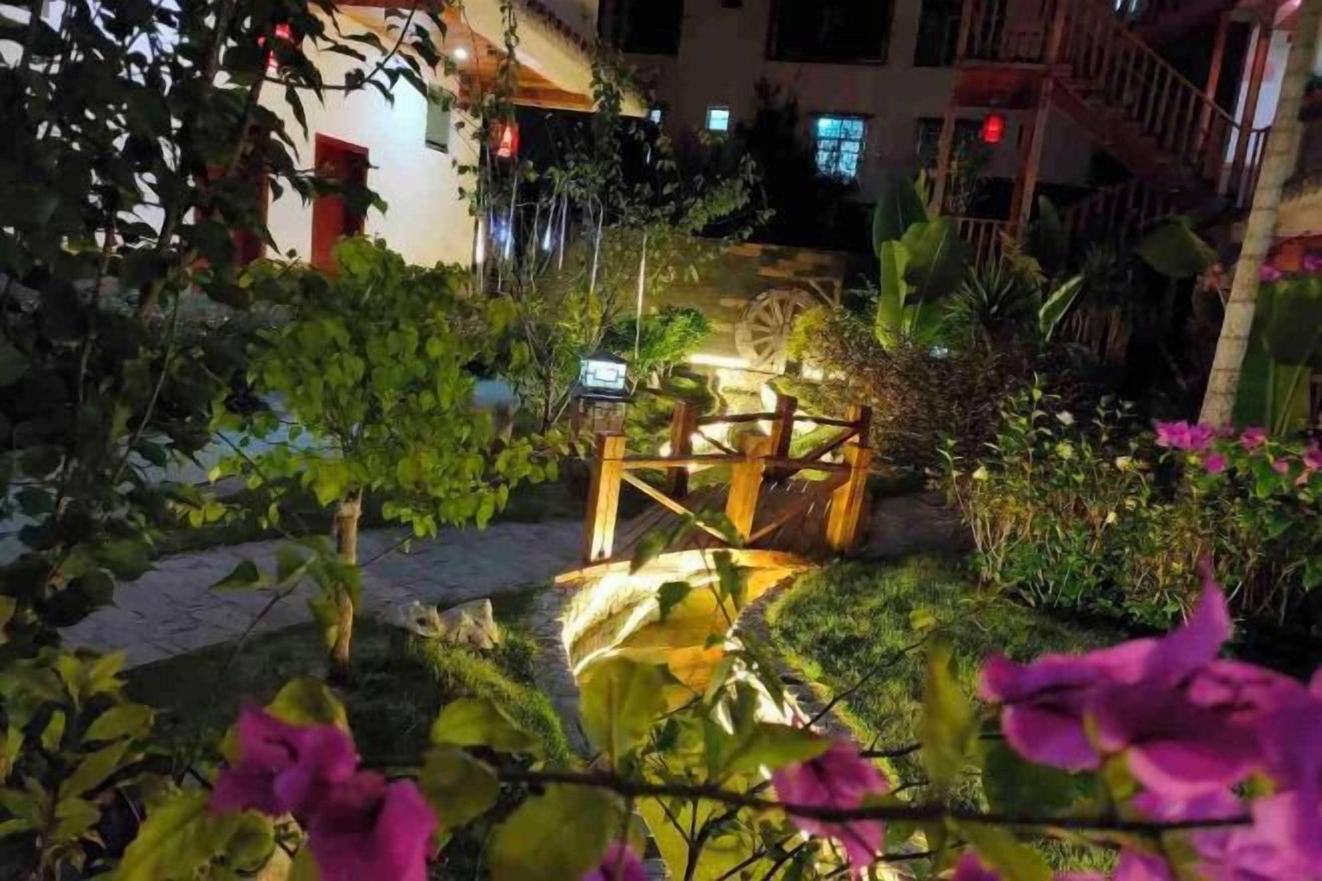 A garden area with a wooden bridge, surrounded by lush greenery and flowering plants.