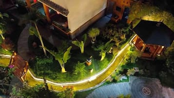 Vista aérea nocturna de un hotel con un sendero curvo, exuberante vegetación y un pequeño pabellón.