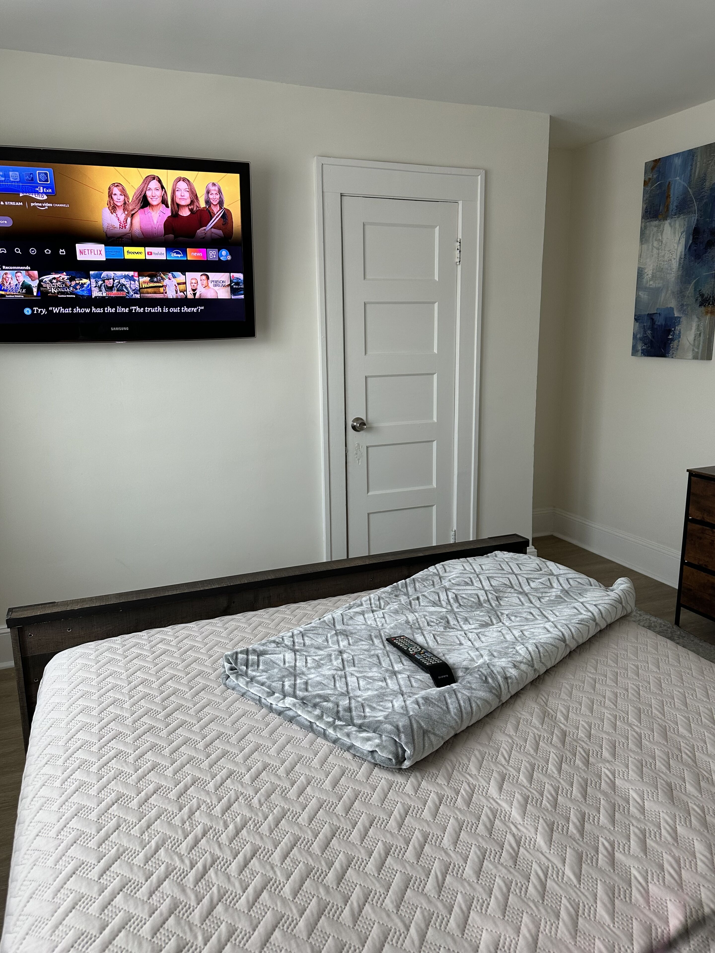 Een slaapkamer met een bed, een aan de muur bevestigde televisie en een deur.