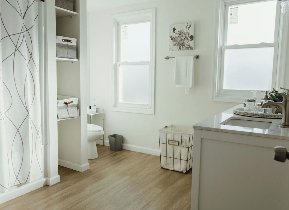 Une salle de bain comprenant des toilettes, un lavabo et un espace douche. Un porte-serviettes est fixé au mur et une poubelle se trouve près des toilettes.