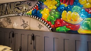 A wall with colorful, abstract art and a partial view of a room with a bed and a door. - Hotel Velero Sur (Iquique)