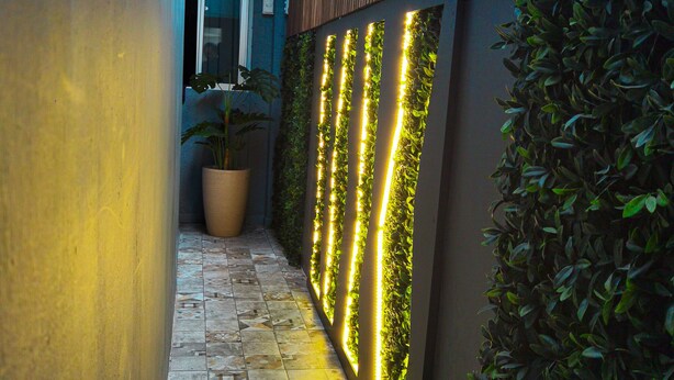 A narrow corridor with patterned tile flooring, vertical LED lights, and a potted plant. - Hotel Velero Sur (Iquique)