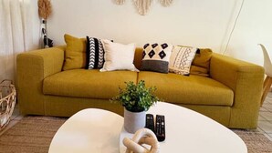 En stue med en sennepsgul sofa, et hvidt sofabord og en vægophængt makramé.