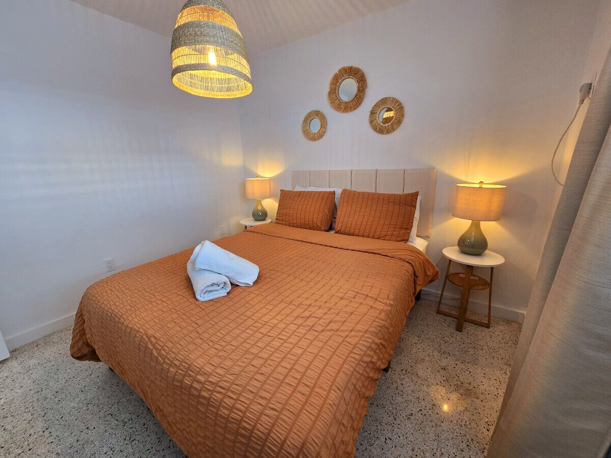 Un lit bien fait, recouvert d’une couverture marron, avec deux lampes de chevet et un mur orné de trois miroirs ronds.
