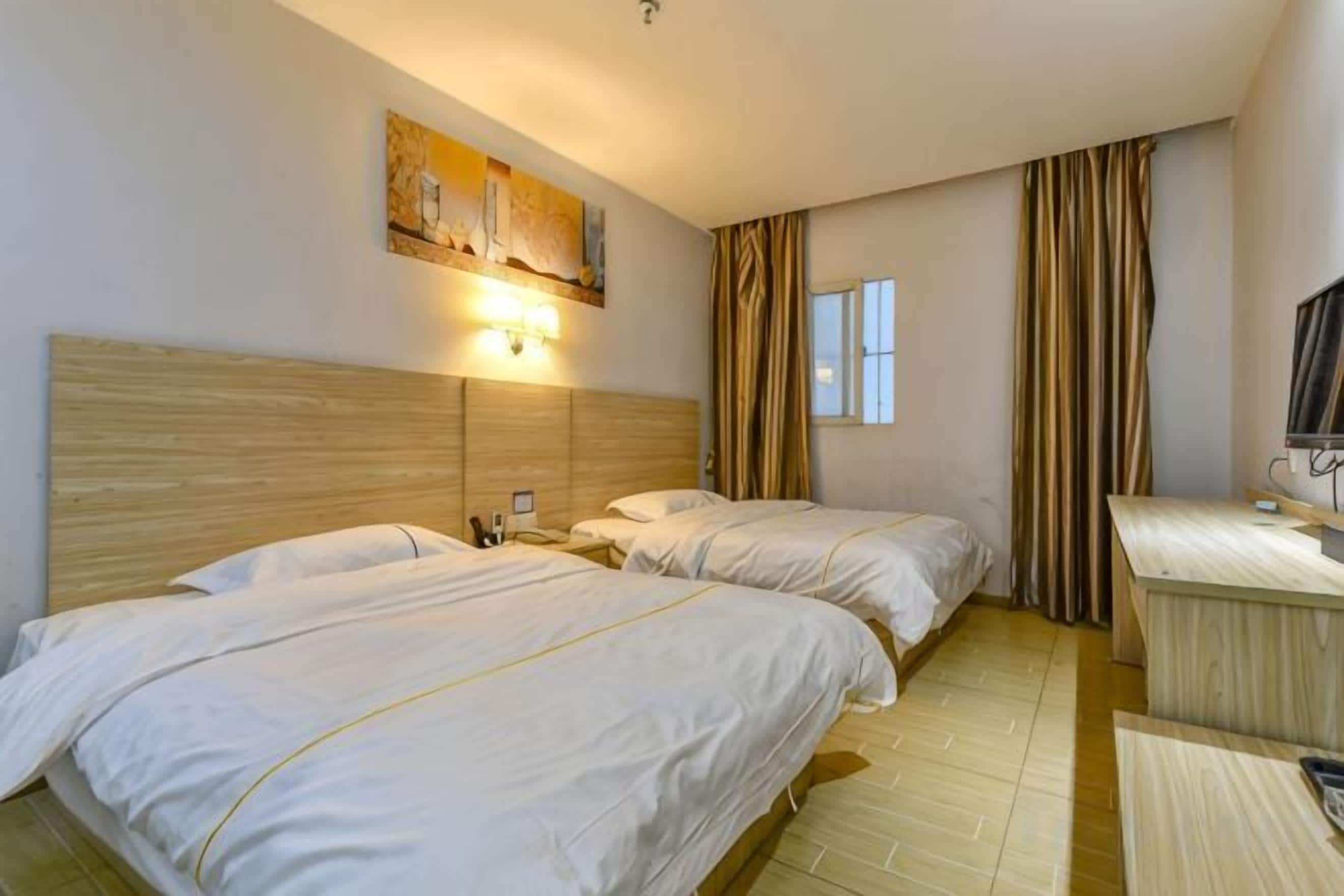 Een hotelkamer met twee bedden, een bureau, een stoel, een televisie en een raam met gordijnen.