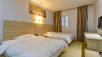 Een hotelkamer met twee bedden, een bureau, een stoel, een televisie en een raam met gordijnen.