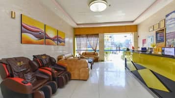 Un vestíbulo de hotel con mostrador de recepción, zona de estar con sillones de masaje y obras de arte en las paredes.