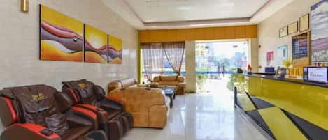 Un vestíbulo de hotel con mostrador de recepción, zona de estar con sillones de masaje y obras de arte en las paredes.
