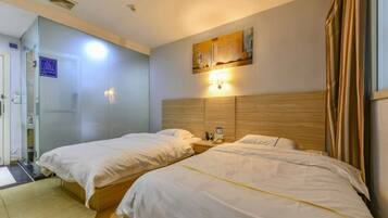A hotel room with two beds, a wooden headboard, a wall-mounted light, and a door leading to a bathroom.