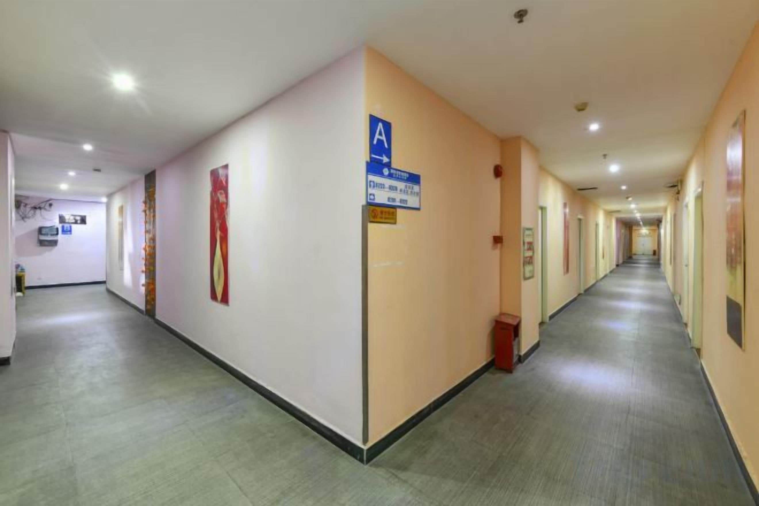 Een lange, smalle hotelgang met vloerbedekking, een blauw bord aan de rechtermuur en deuren aan beide kanten.