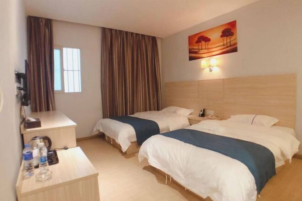Hotellihuone, jossa on kaksi sänkyä, työpöytä, jossa on puhelin, vesipullo ja taulu seinällä.