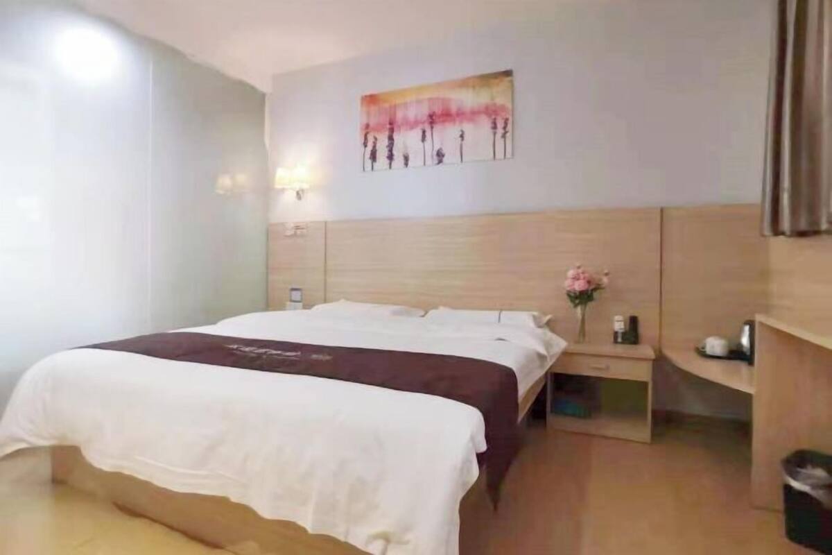 Hotellihuone, jossa on sänky, yöpöytä ja taulu seinällä.