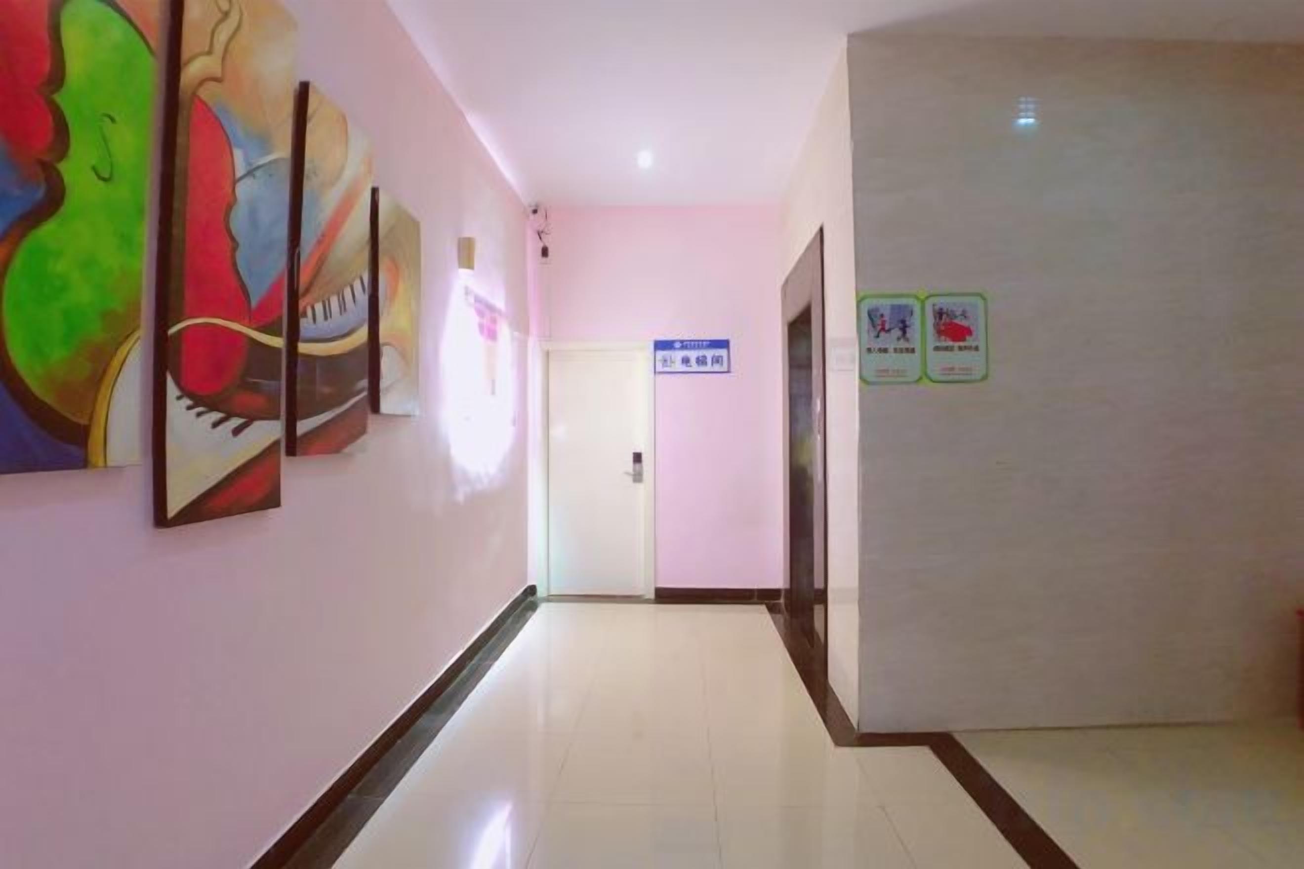 A hallway with a door at the end, a sign on the wall, and artwork on the left.