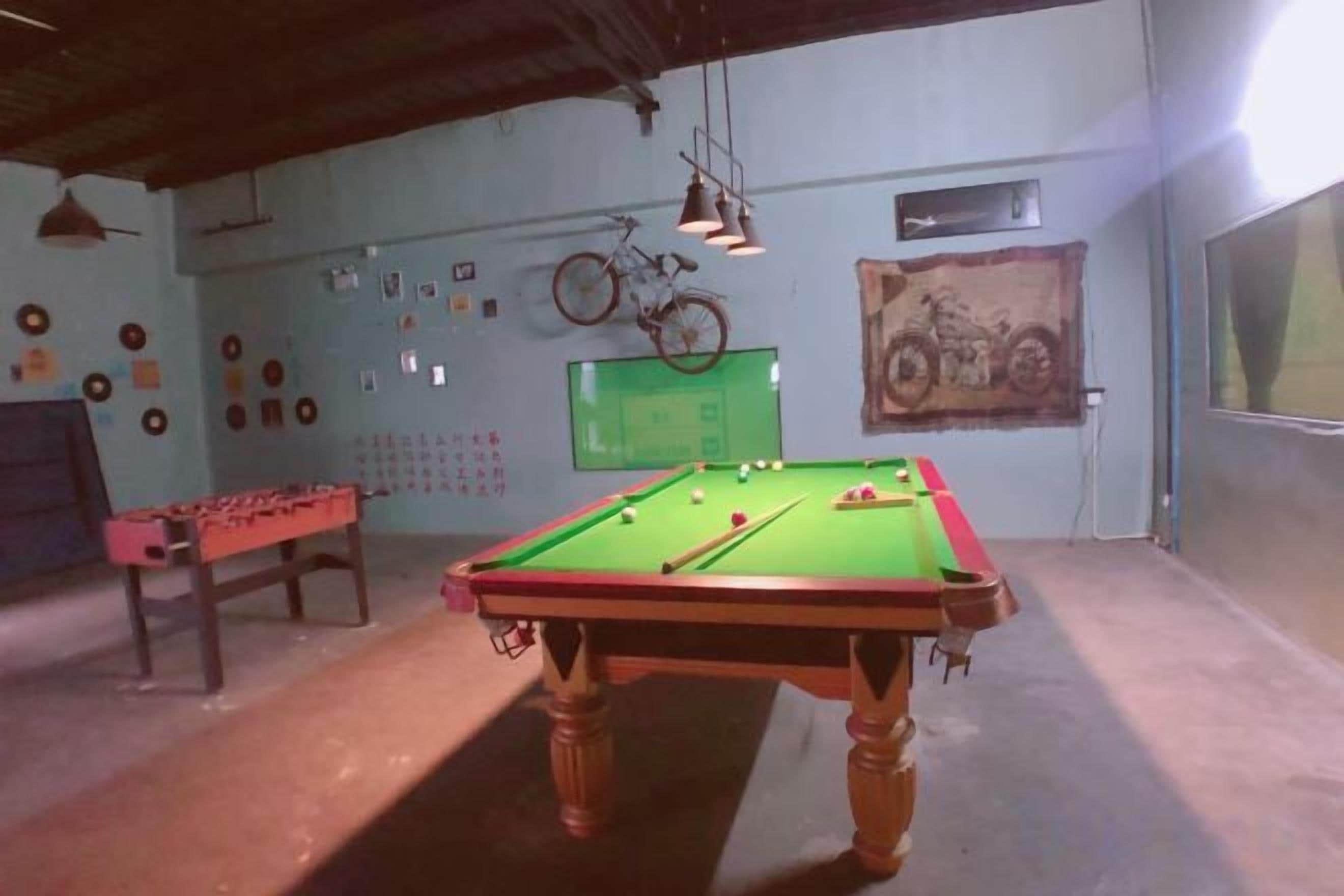 Une table de billard dans une pièce où l’on peut voir un vélo accroché au mur, une table de baby-foot et divers éléments de décoration murale.