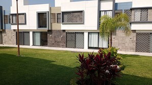 A modern building with multiple windows, a well-maintained lawn, and a small palm tree. - Beautiful and Spacious House Alcatraz, Florencia Gardens, Cuernavaca (Cuernavaca)