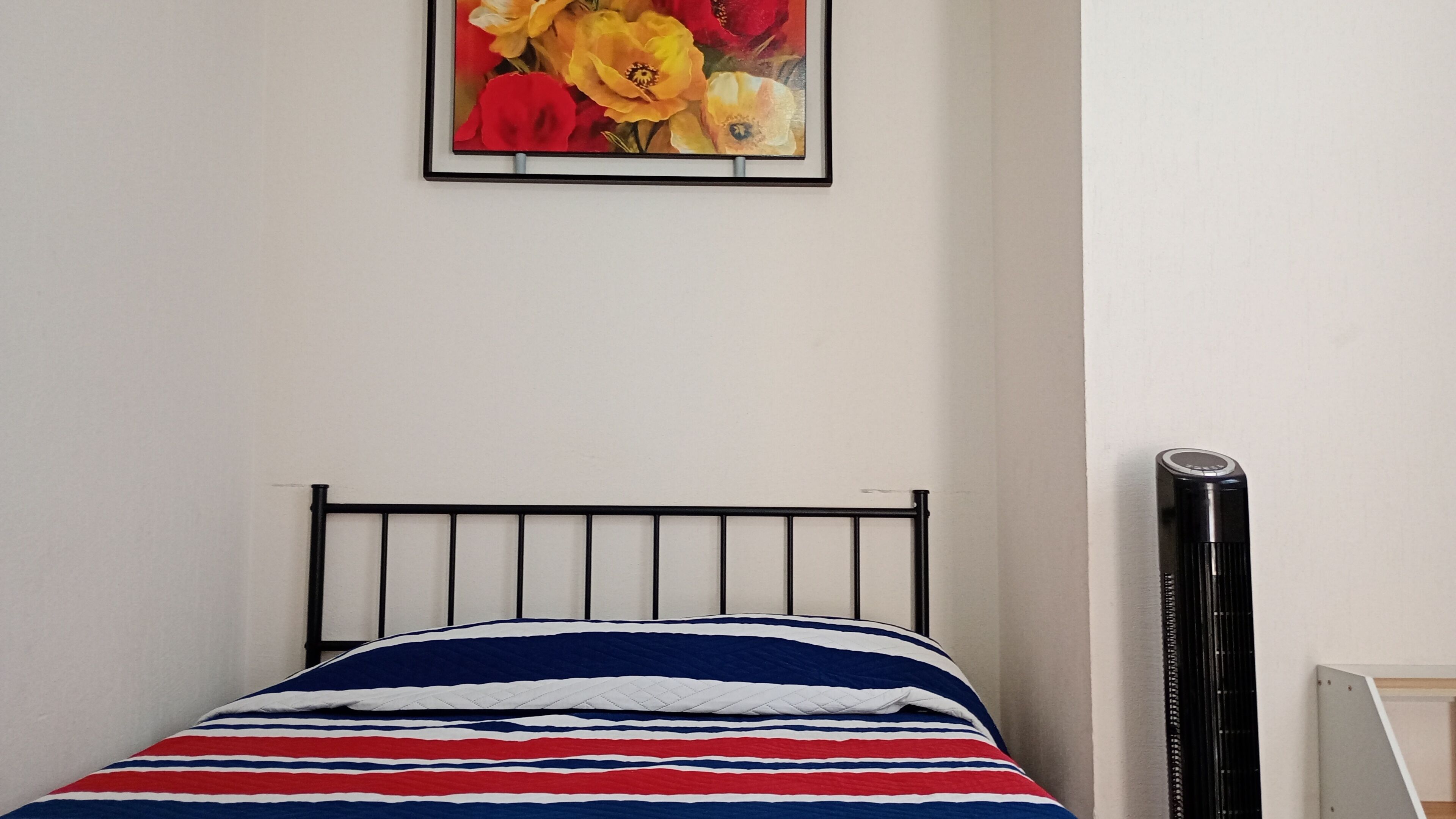 A bed with a striped bedspread, a black metal headboard, and a framed floral artwork on the wall.