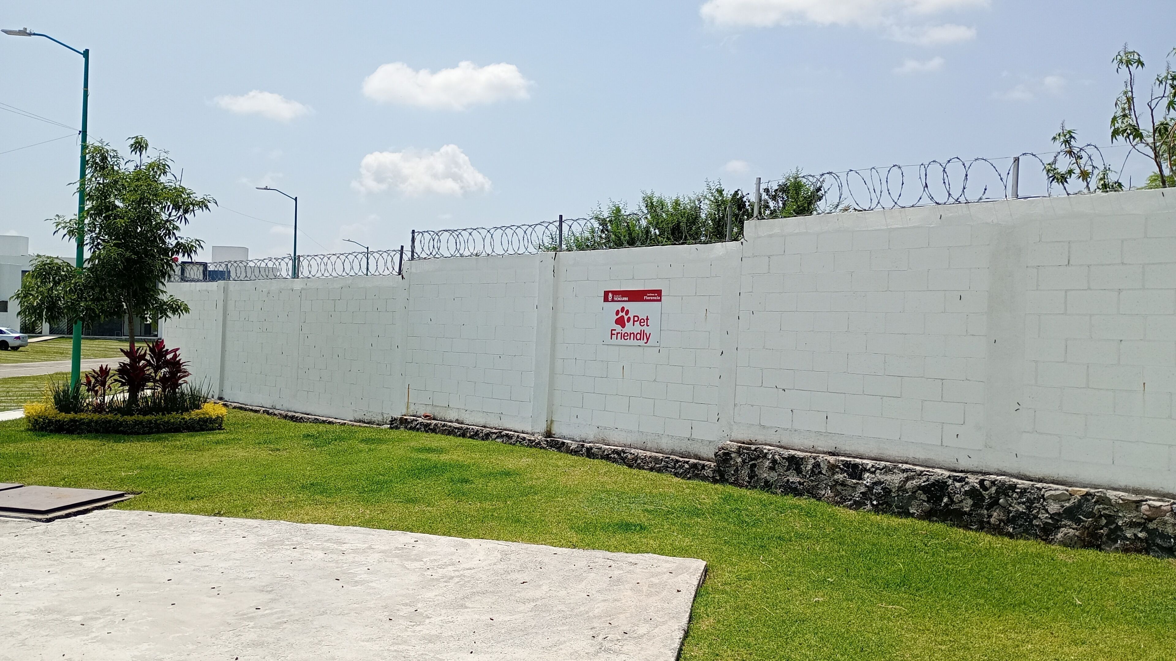 A white brick wall with a 'Pet Friendly' sign, a barbed wire fence, and a street lamp.