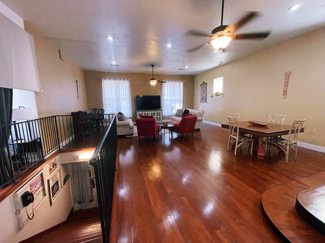 A spacious living area with a wooden floor, a dining table with chairs, a sofa, and a television.