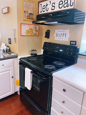 A kitchen with a black stove, white cabinets, and a sign that says 'let's eat.'
