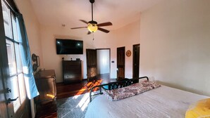 Un dormitorio con cama, ventilador de techo, cómoda, televisor y puerta.