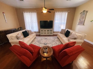 A living room with two sofas facing each other, a coffee table in the center, a ceiling fan, and a television on the wall.