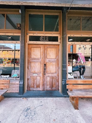 A wooden double door with the number 611, a bench outside, and a mannequin in the window. - The Landing at Main Street Suites (Van Buren)