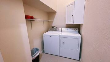 A laundry room with a washing machine and dryer, a trash bin, and a cabinet.