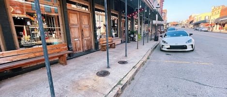 A street with a row of shops, a bench, and a parked car.