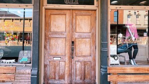 Una puerta doble de madera con el número 611 en la parte superior, una pequeña ventana con un letrero arriba y un banco en el exterior.