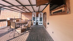 Un patio techado al aire libre con una mesa y sillas de madera, una parrilla y un muro de ladrillo al fondo.