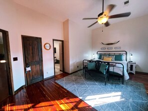 A bedroom with a bed, bedside tables, a ceiling fan, and a view of a hallway.