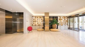A modern lobby with a wooden floor, a red chair, a large potted plant, and a glass wall with a view. - JI Hotel (Beijing South Railway Station Jiaomen East Subway Station) (Beijing)