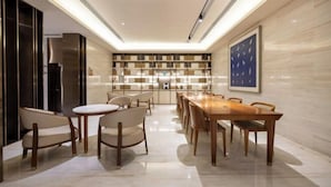 A modern dining area with a long wooden table and chairs, a kitchen in the background, and a large framed artwork on the wall. - JI Hotel (Beijing South Railway Station Jiaomen East Subway Station) (Beijing)