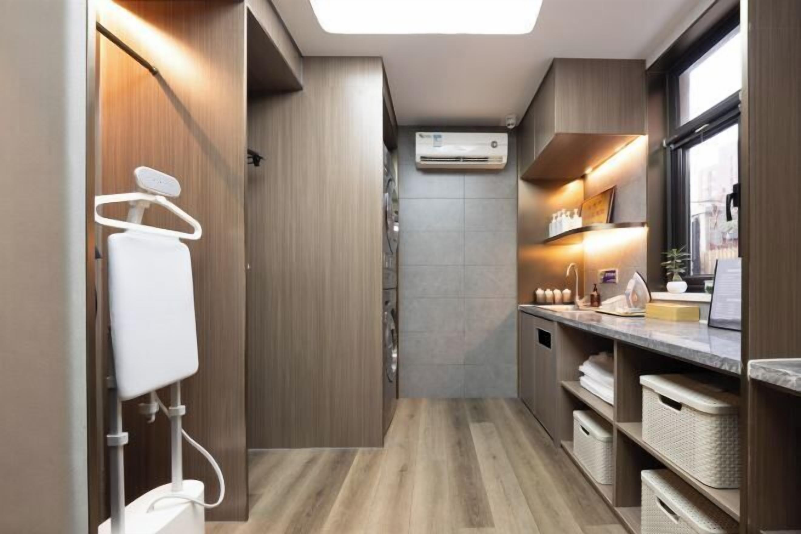 A compact kitchen with a built-in air conditioner, a hanging drying rack, and storage shelves.