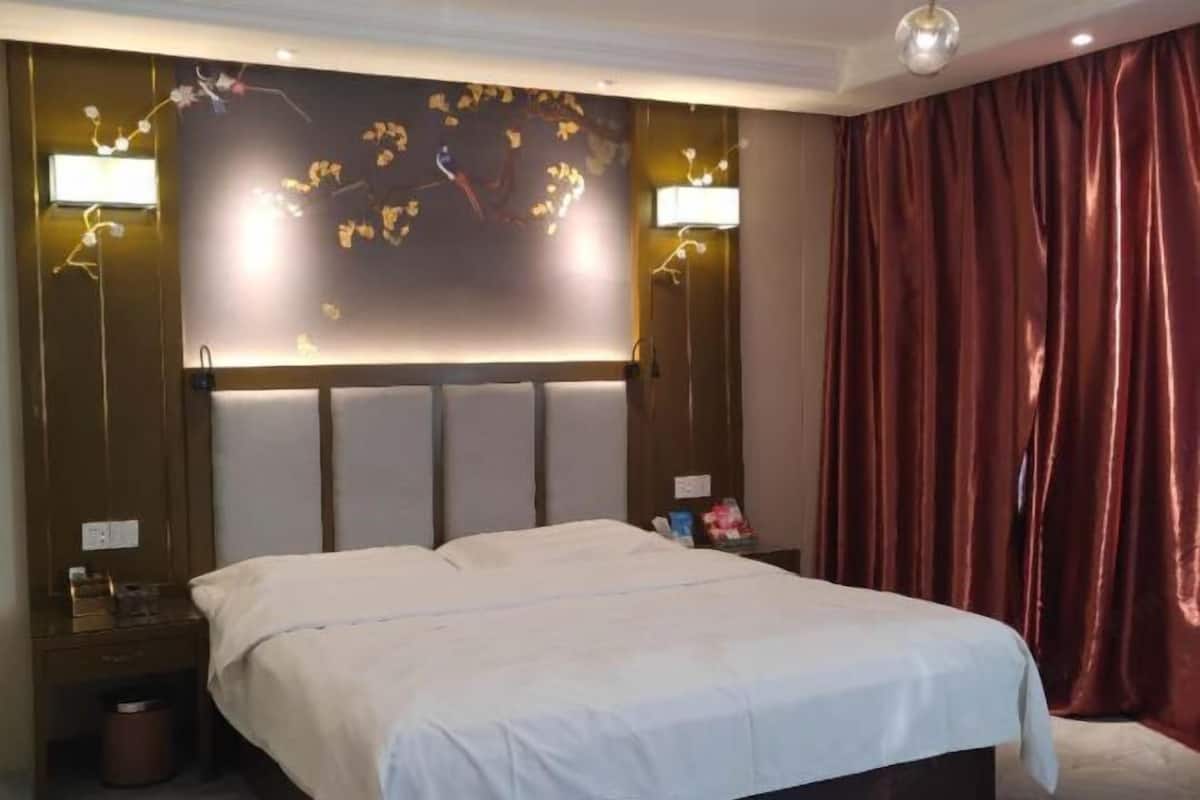 A hotel room with a bed, a nightstand, a wall-mounted light fixture, and a curtain.