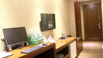 A hotel room with a desk, computer, television, and a door.