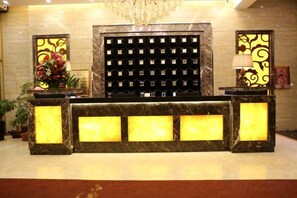 A reception desk with a marble top, a black decorative panel, and a chandelier above. - Wanhao Business Hotel (Baiquan)