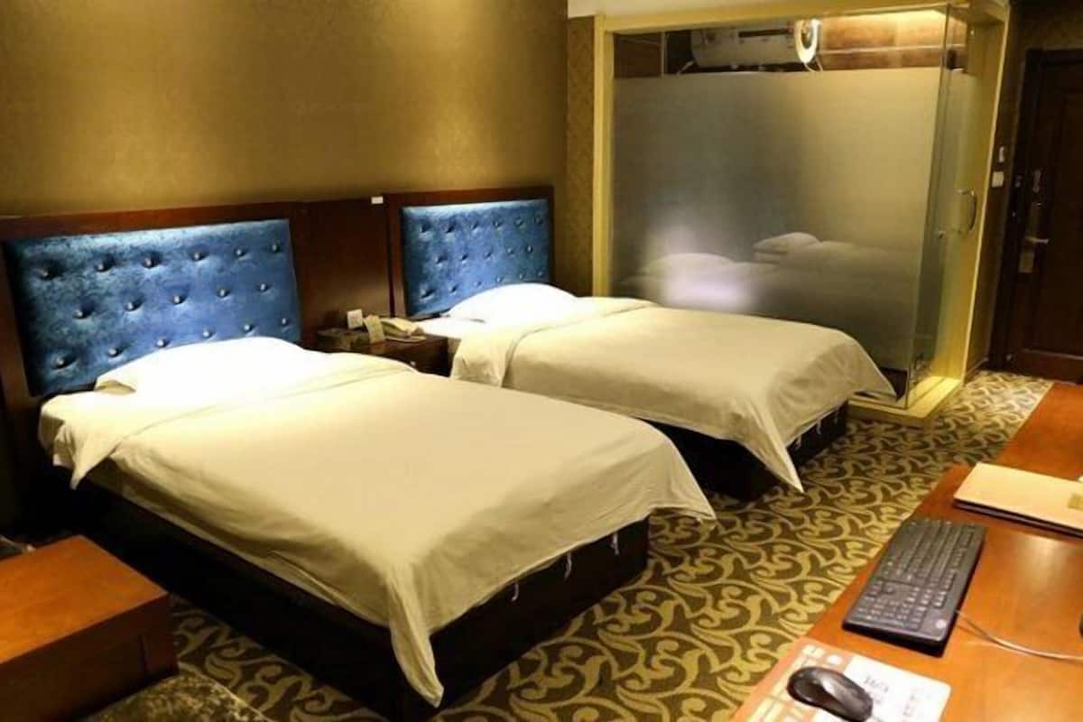 A hotel room with two beds, a desk with a computer, and a wardrobe.