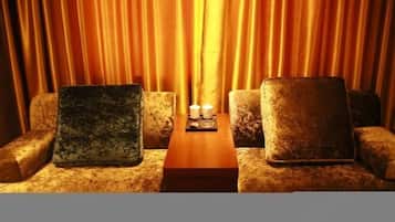 A seating area with a wooden table and two candles, set against a backdrop of golden curtains.
