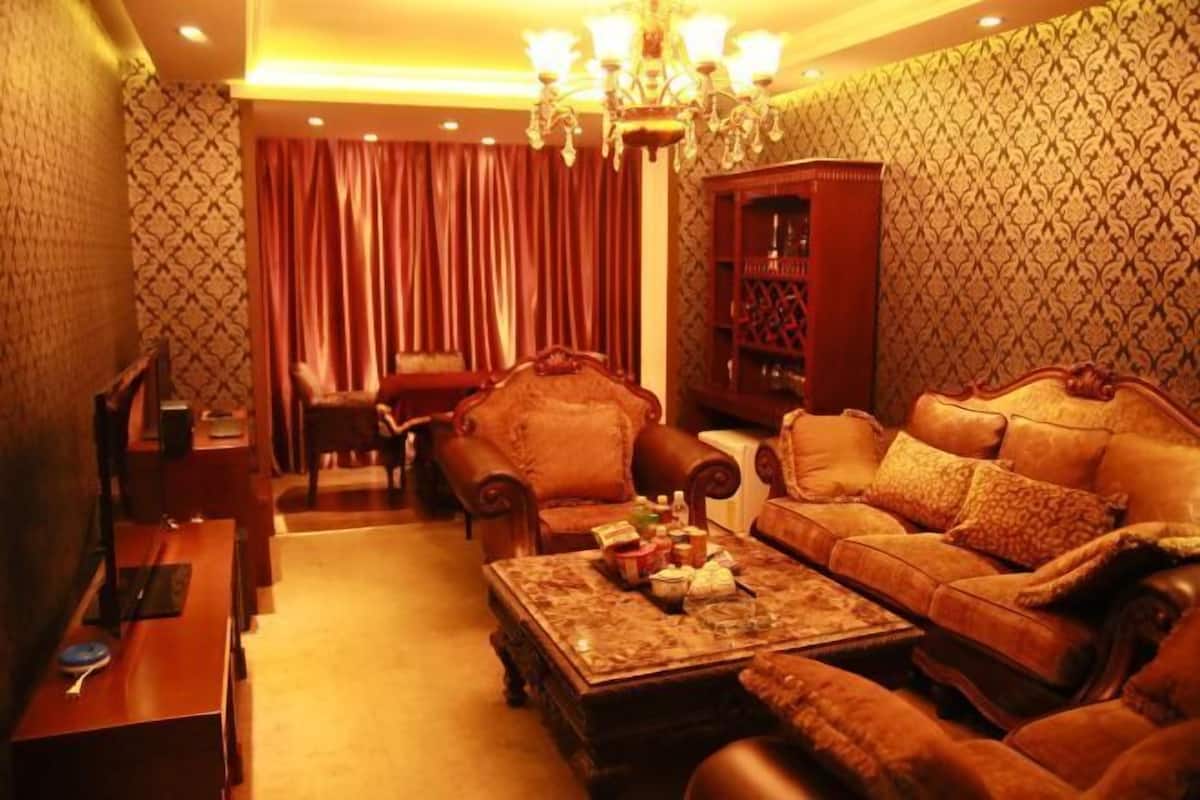 A cozy living room with a sofa, armchairs, a coffee table, a bookshelf, and a chandelier.
