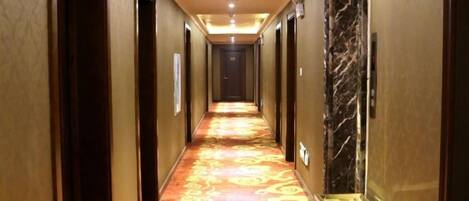 A hotel hallway with a patterned carpet, doors on both sides, and a marble wall on the right.