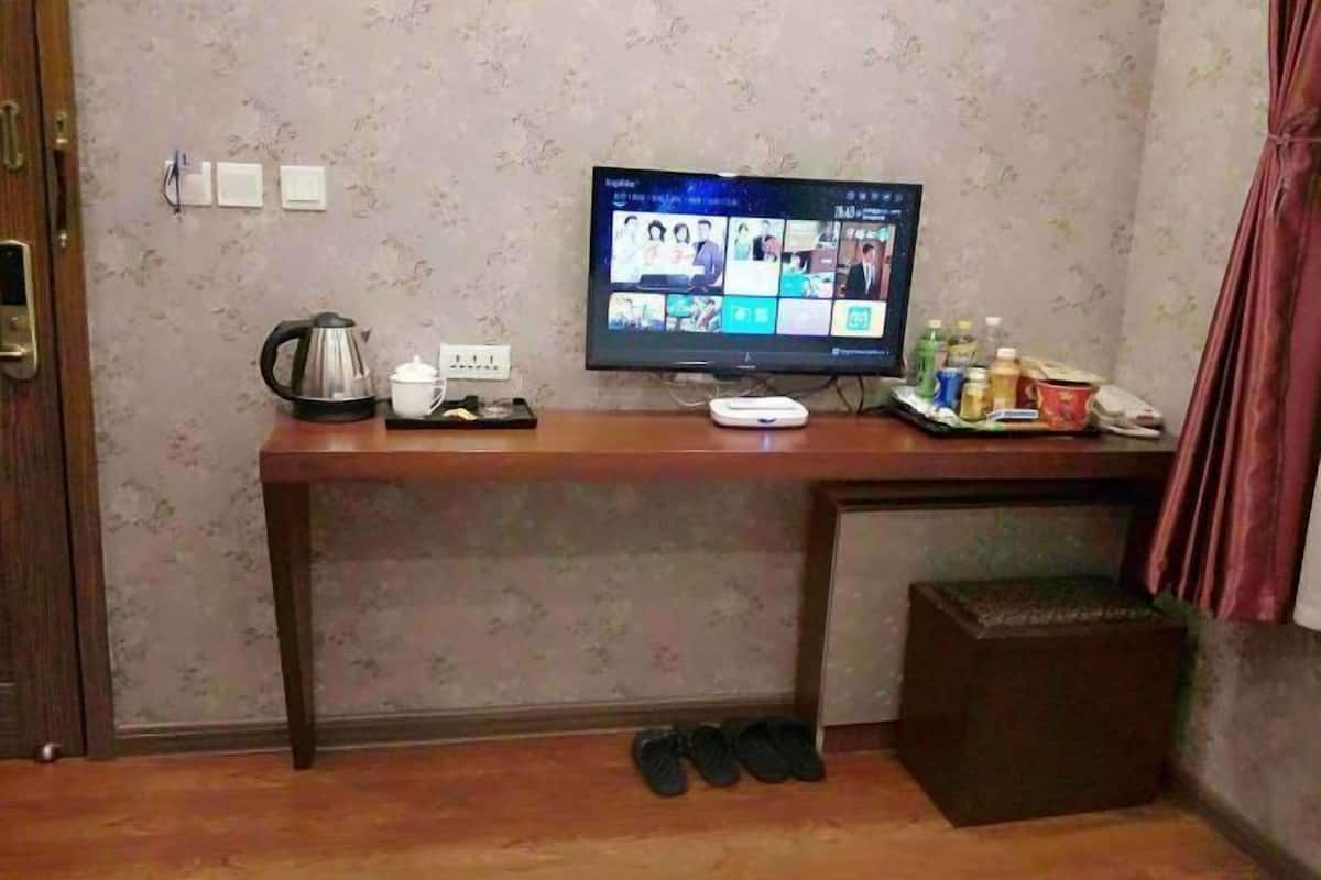A room with a wooden desk, a television, a kettle, and a small trash bin.