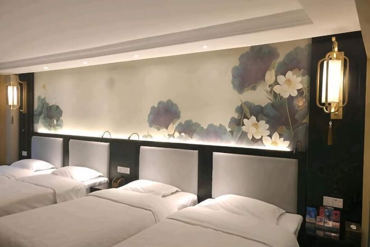 A hotel room with two beds, a floral wall mural, and a wall-mounted light fixture.