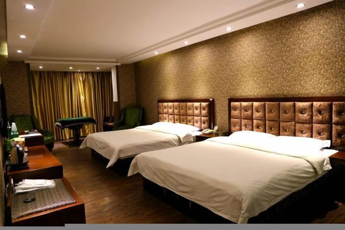 A hotel room with two beds, a desk, a chair, and a large window with curtains.