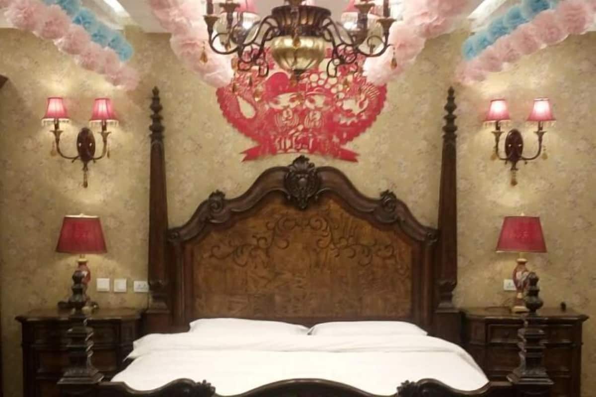A room with a wooden bed, wall sconces, a chandelier, and a decorative ceiling.