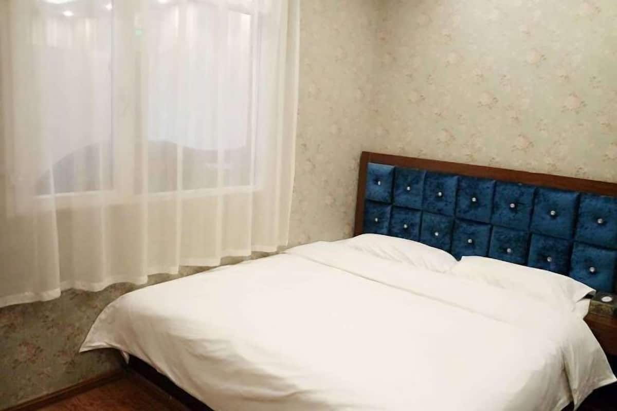 A bedroom with a bed, a window with sheer curtains, and a floral wallpaper.
